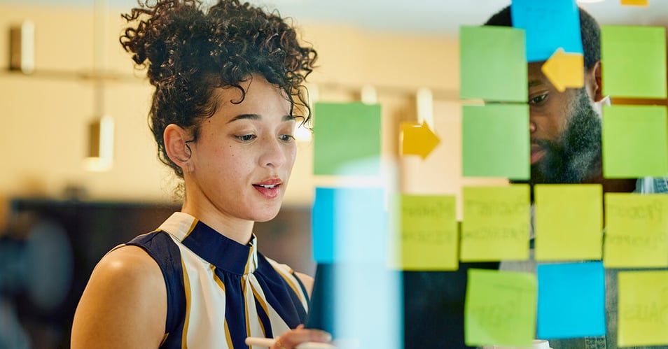 image of two professionals using sticky notes on a clear whiteboard to map out processes in their office