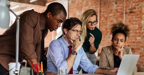 an image of a group of coworkers around a laptop evaluating business processes 