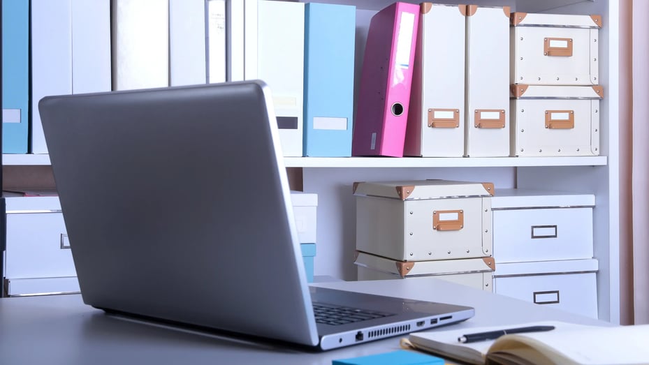 image of a computer on a desk next to shelves full of paper student records