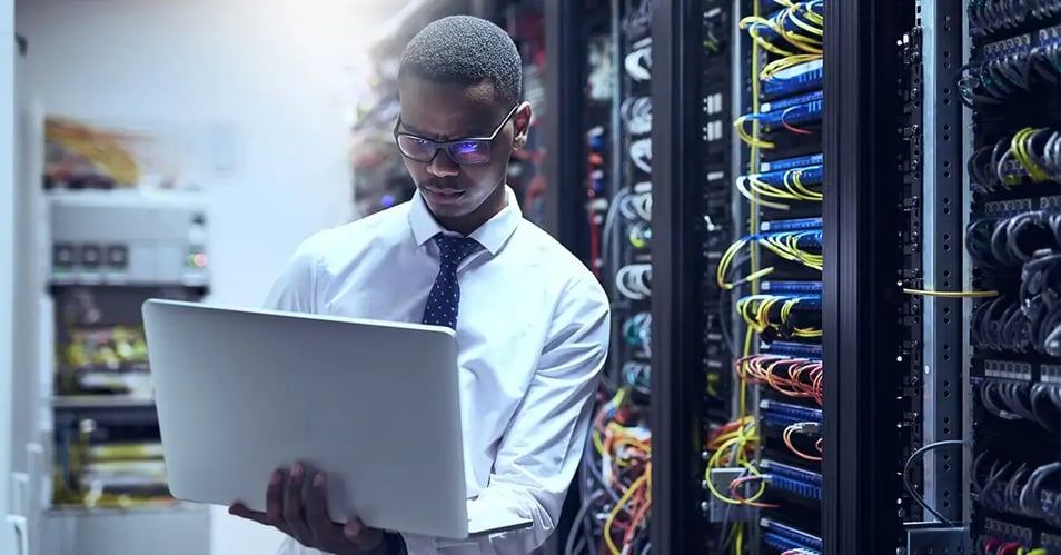image of an IT professional reviewing a document on his laptop in a server closet 