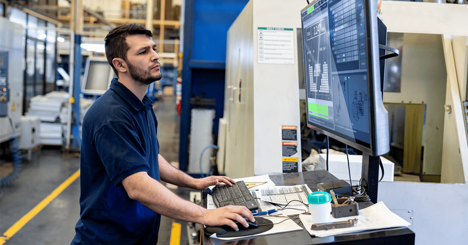 an image of a manufacturing professional working on a desktop computer in a warehouse