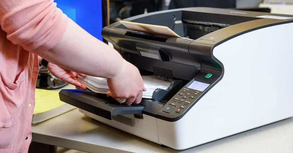 An office worker feeding a stack of documents into a professional scanner, representing the first step of scanning automation and digital transformation.