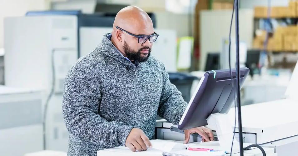 A print production manager using a digital interface to manage a hybrid print workflow in a modern commercial printing facility.