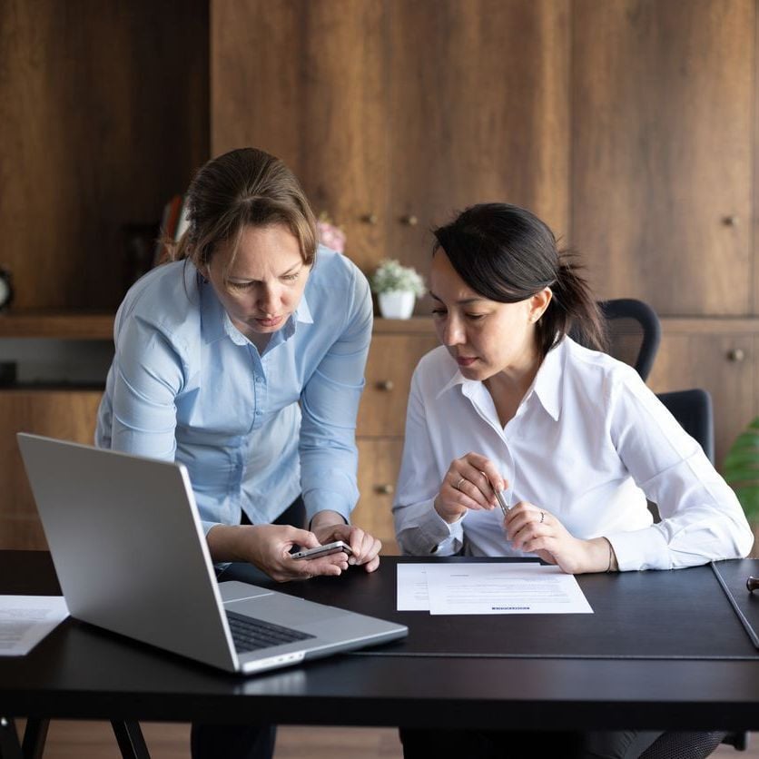 image of two government workers discussing documents via paper mobile and laptop