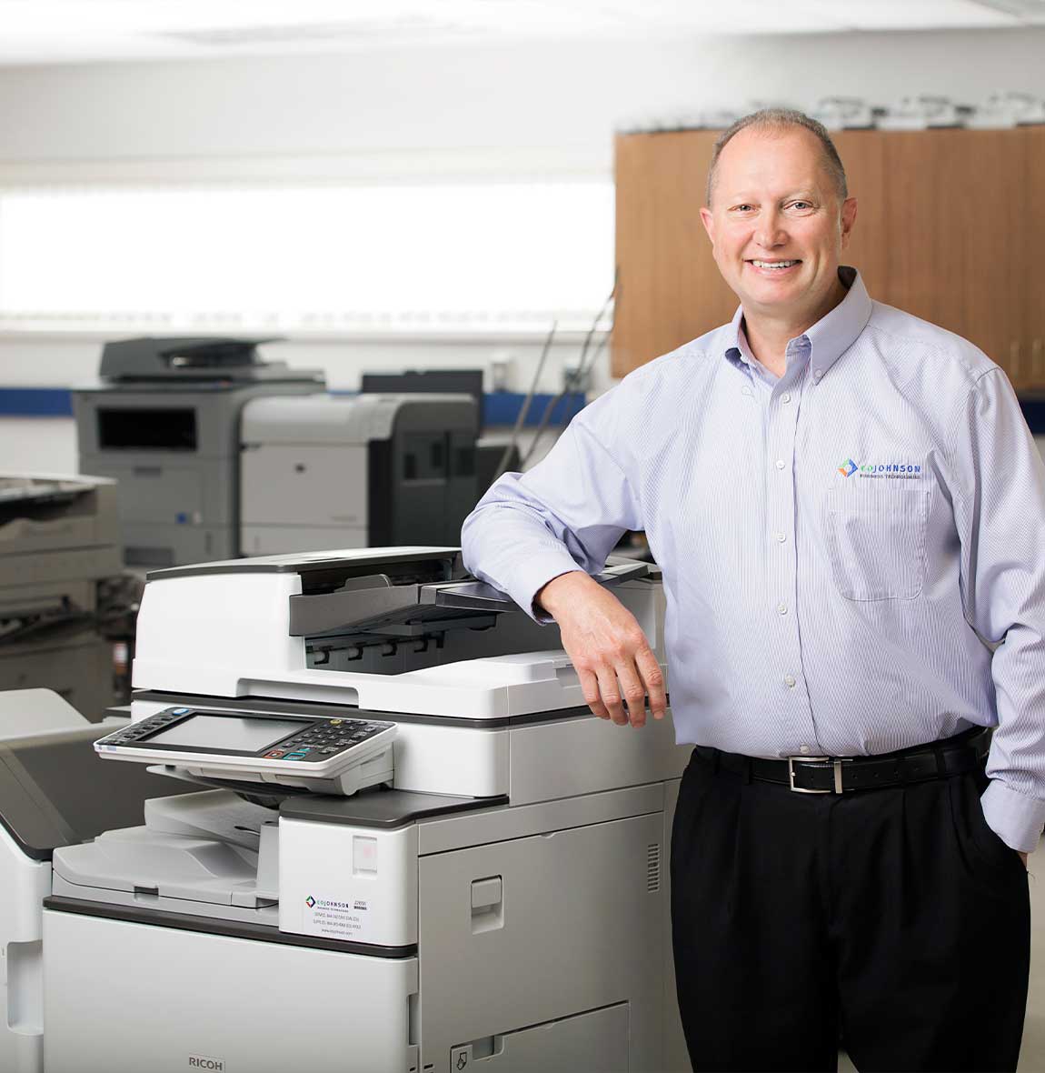 eo johnson employee smiling next to ricoh copier