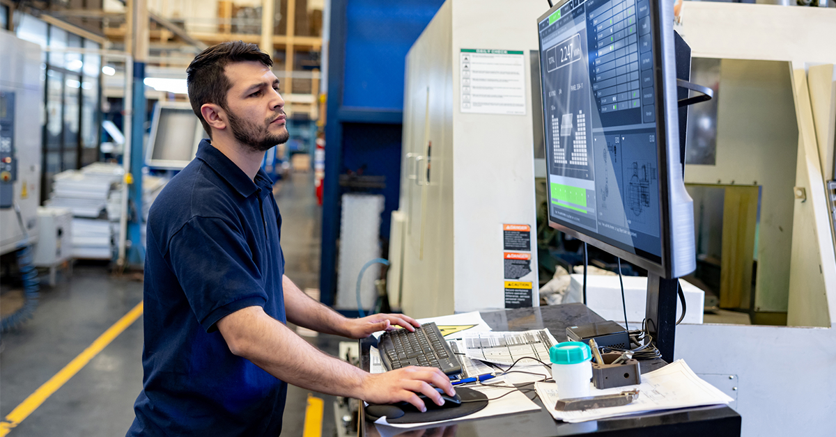 an image of a manufacturing professional working on a desktop computer in a warehouse