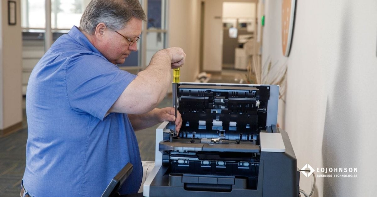 A technician repairs a business copier in a professional office setting, highlighting the importance of service agreements when buying or leasing a copier.